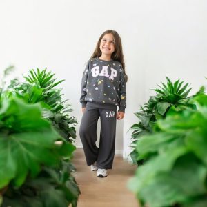 A young girl wearing a dark grey GAP sweatshirt with floral patterns and matching wide-leg joggers.